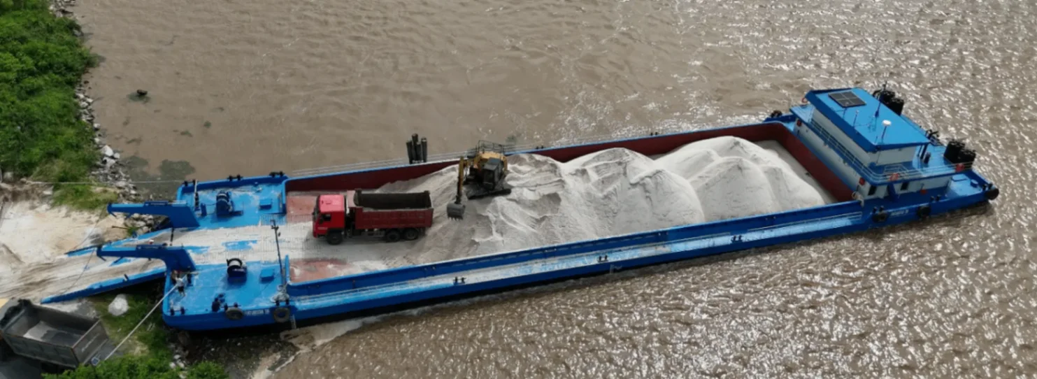 Blue barge carrying white sand with an excavator and truck on the river
